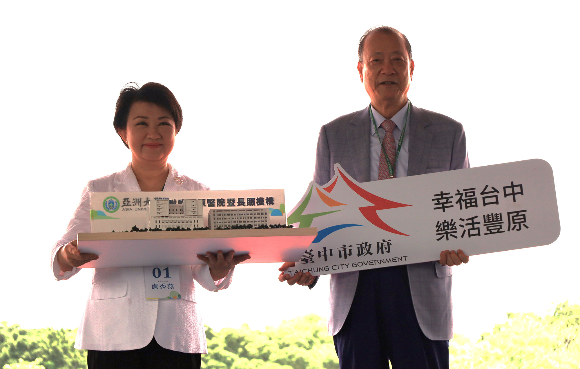 Mayor Hsiu-Yen Lu of Taichung City (left) and the founder of Asia University, Chang-Hai Tsai (right), exchanging tokens, symbolizing the construction of the "Asia University Fengfu Health Park" as a representation of "Happy Taichung, Lively Fengyuan"