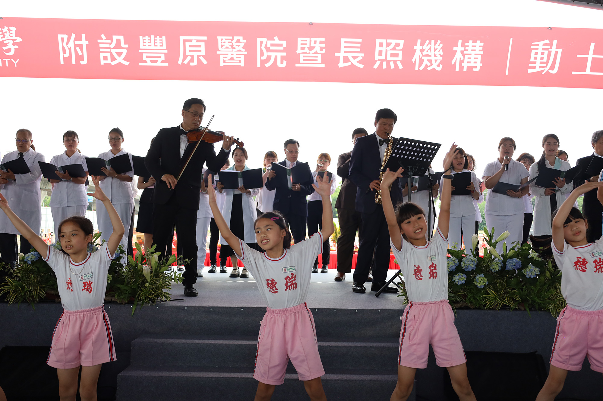 The groundbreaking ceremony of the "Asia University Fengfu Health Park," featuring President Jeffrey J.P. Tsai of Asia University (middle back), Director Feng-Yuan Chang of the Economic Development Bureau of Taichung City (left middle), Director Tzu-Chan Tseng of the Health Bureau of Taichung City (right middle), and elementary school children from Ruisui singing "I Believe" together